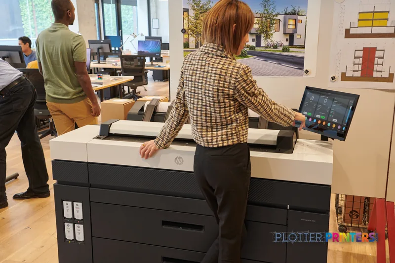 Woman operating HP DesignJet XL 3800 36-in printer in office setting with architectural designs displayed