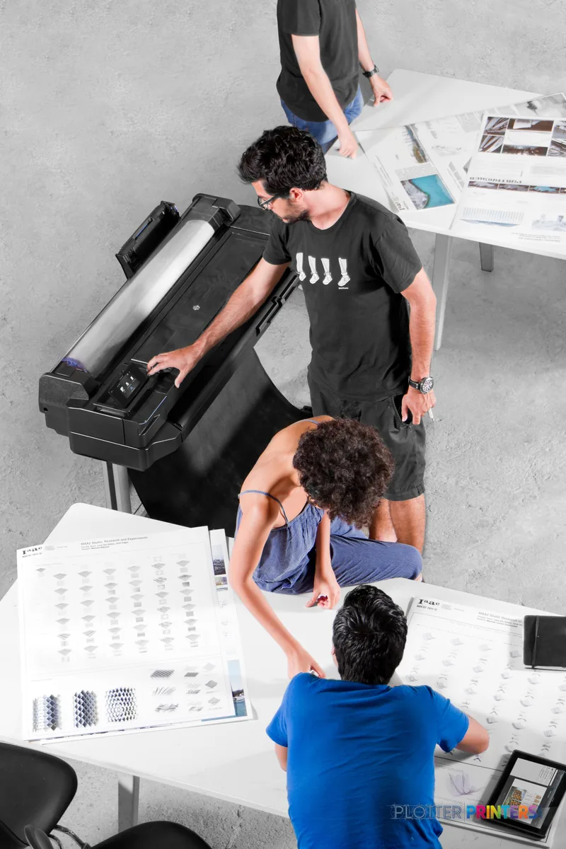 HP Designjet T520 lifestyle image showing three people examining large format prints around the printer in an office setting