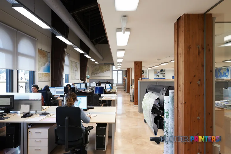 HP Designjet Z6800 large format printer lifestyle image showing the black printer in a busy office workspace with staff at d…