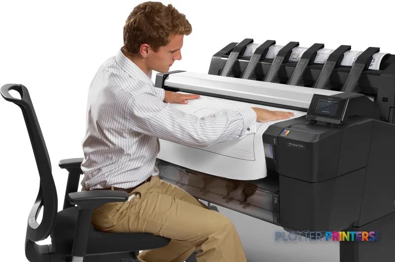 Man seated at HP Designjet T2530 large-format printer, feeding wide paper into the device in a lifestyle setting
