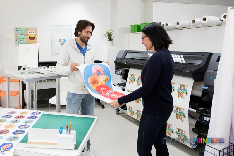 HP Latex 335 Print and Cut Solution lifestyle image showing two people examining a colorful printed sticker in a studio work…