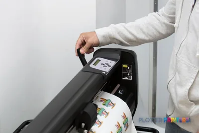 HP Latex 315 Print and Cut Solution lifestyle image showing a person operating the grey printer's control panel while colorf…