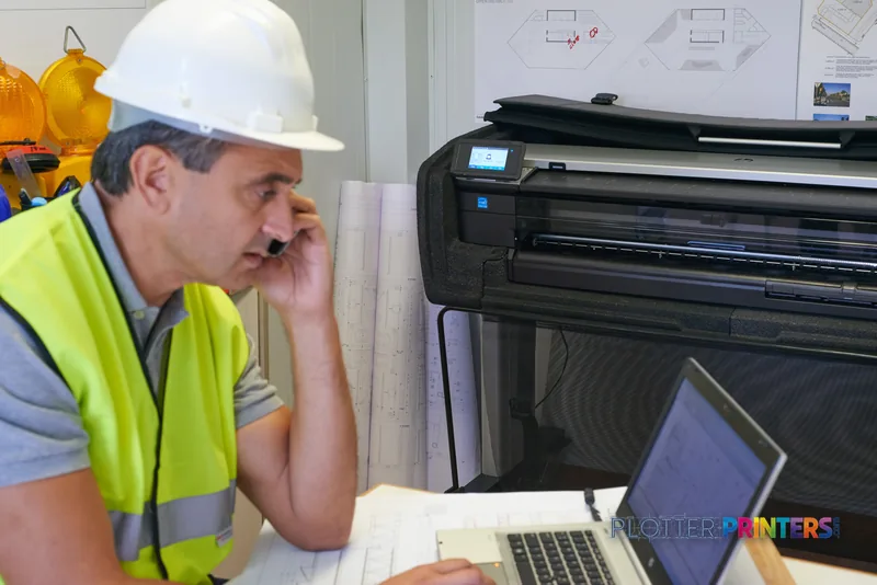 HP DesignJet T830 large format printer in a construction office setting with a worker in safety gear