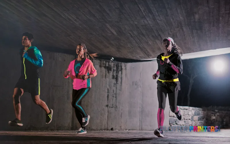 Three runners in neon athletic wear jogging in an underground concrete tunnel at night
