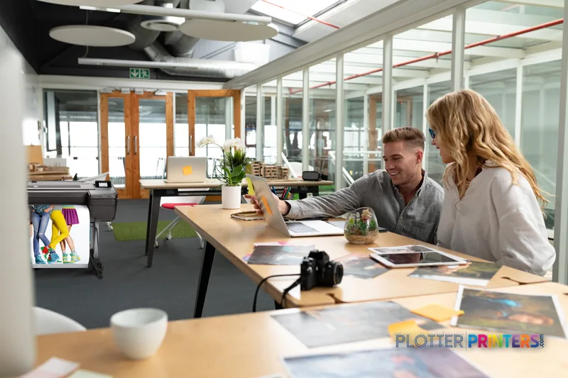 HP DesignJet Z9+ 24-in PostScript Printer lifestyle image showing the black printer in a modern office workspace with two pr…