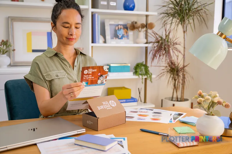 Woman unboxing HP DesignJet T2600 36-in PostScript Multifunction Printer at desk with printed samples