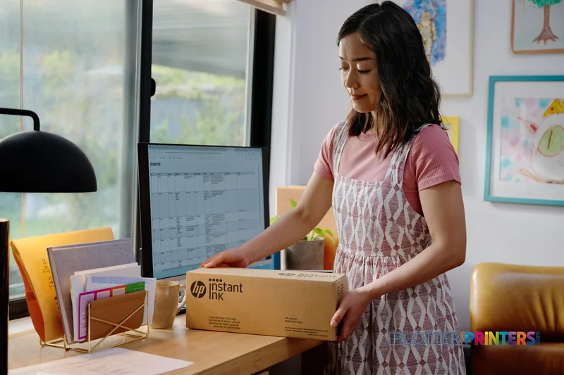 Woman in home office holding HP Designjet T2600 ink box, lifestyle view with desk and computer